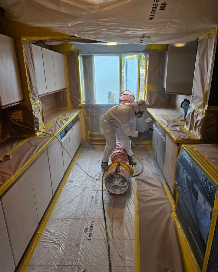 A sprayer in a protective suit and mask spraying a galley kitchen